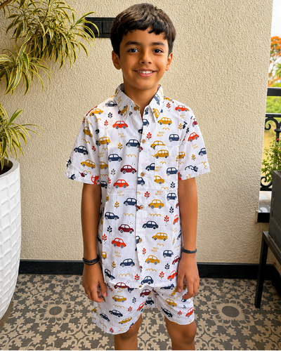 A toddler standing in balcony wearing Aruvo's premium cotton white co-ord set, with beautiful cars printed on it