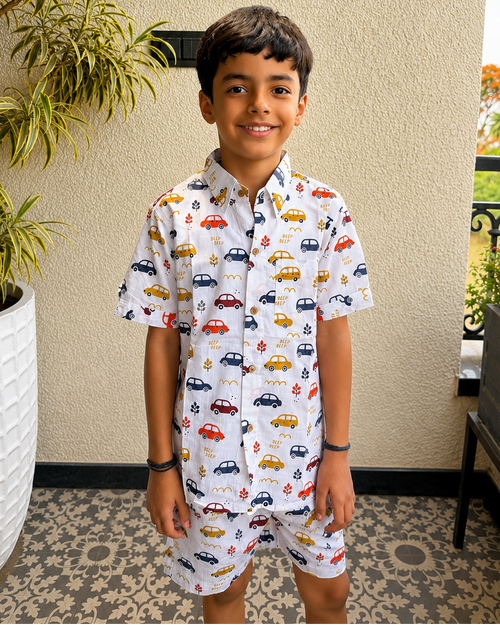 A toddler standing in balcony wearing Aruvo's premium cotton white co-ord set, with beautiful cars printed on it