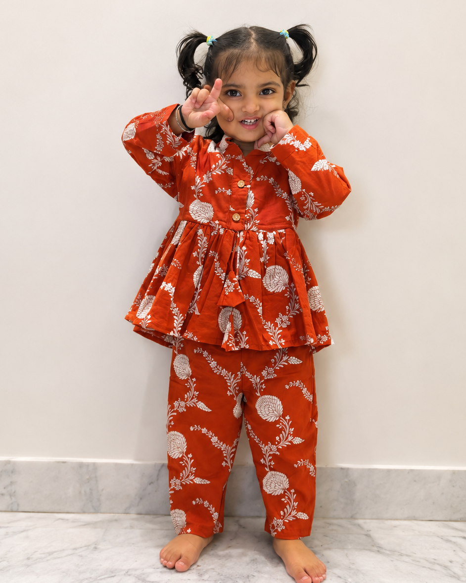 Child in rust Dori Co-ord dress from Aruvo with white patterns standing on near the wall