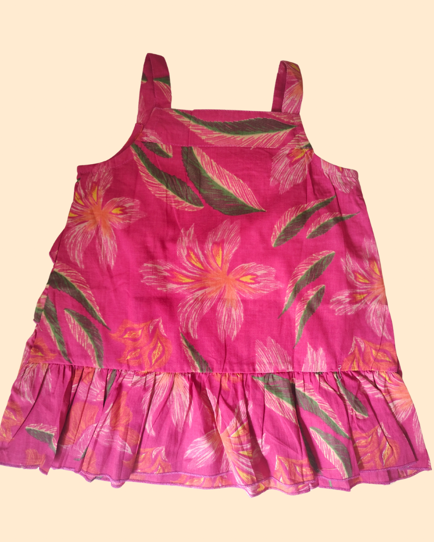 A pink tiered sleeveless dress with a tropical floral and leaf print, featuring wide shoulder straps and a ruffled hem, shows back side of the top.