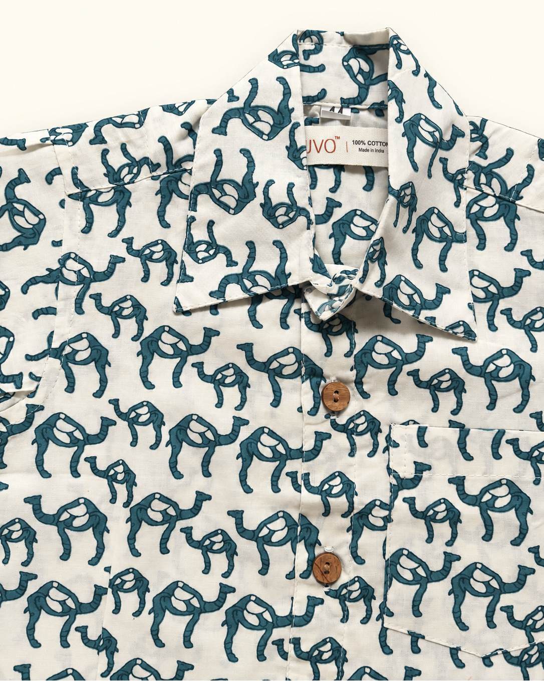 A close-up of a white short-sleeve button-up shirt with an all-over dark teal camel print, featuring brown buttons and a visible 'ARUVO' brand label inside the collar.