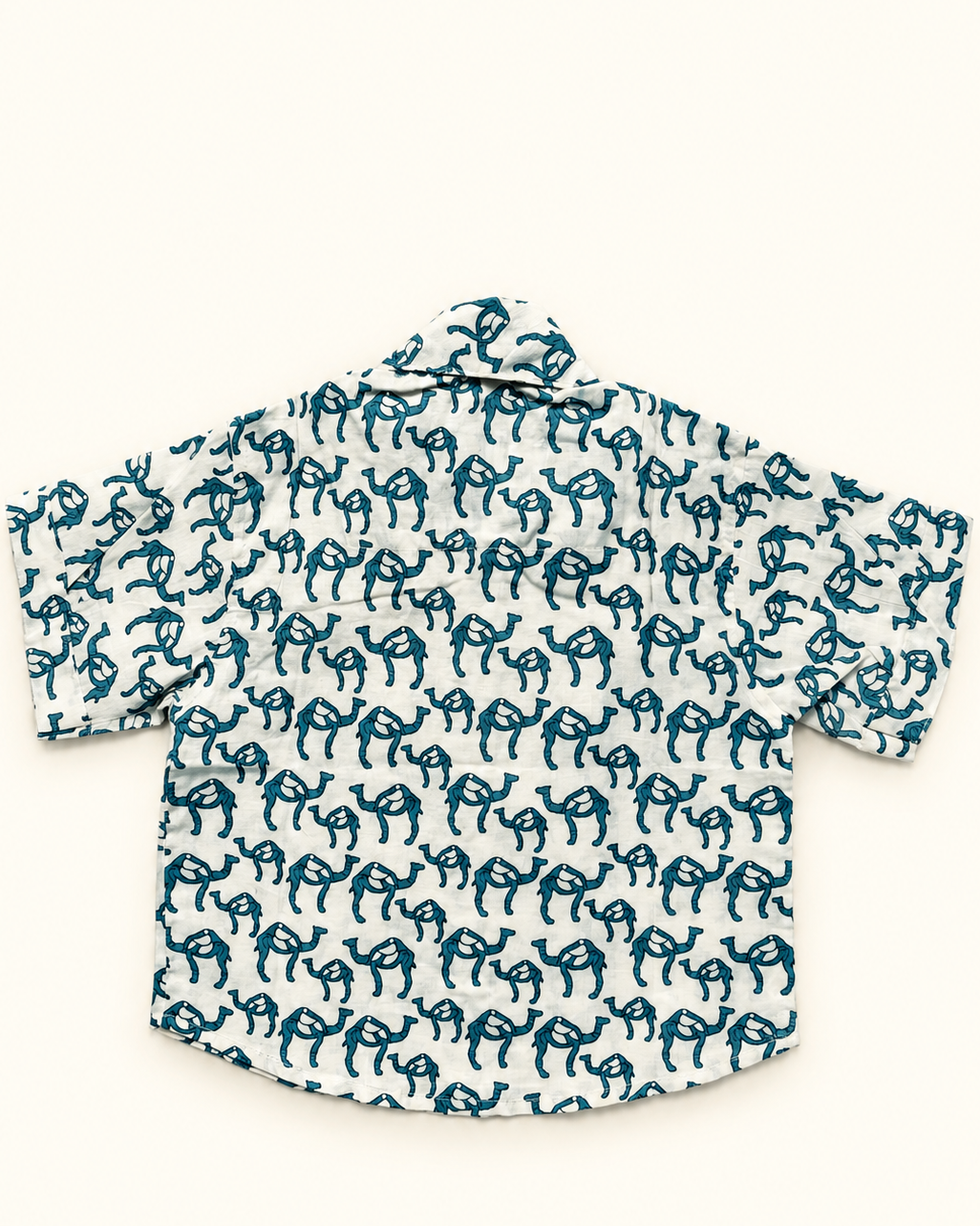 A short-sleeve button-up shirt with a white base and an all-over teal blue hand-drawn style animal print, laid flat against a light cream background.