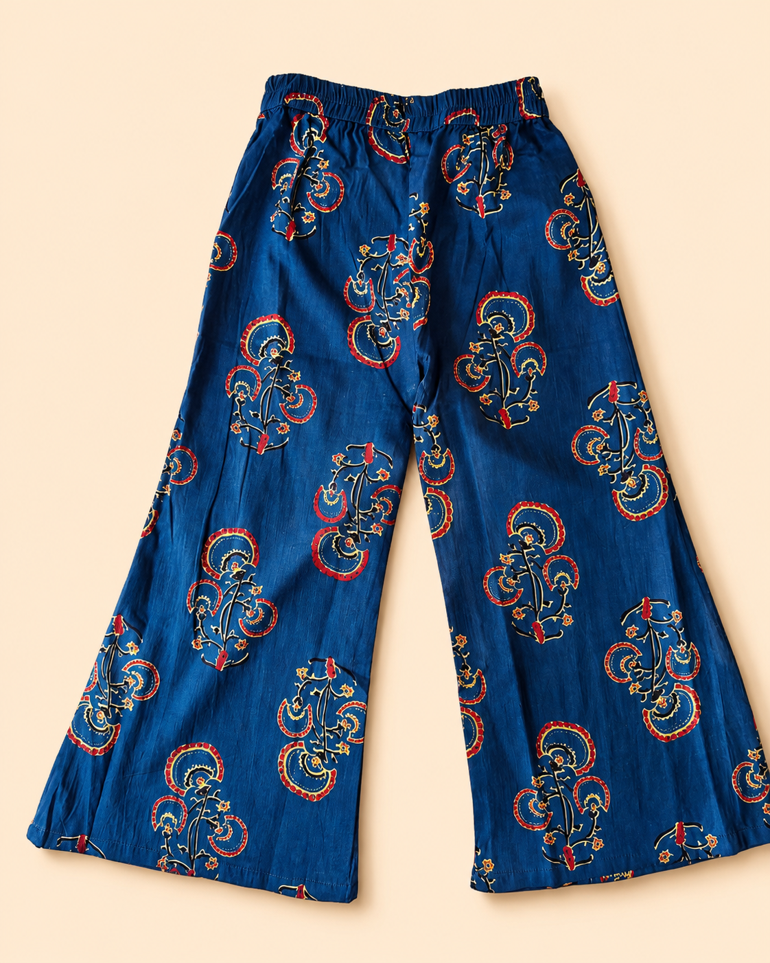 Blue wide-leg pants with an all-over red and gold paisley block print, laid flat on a light beige background.