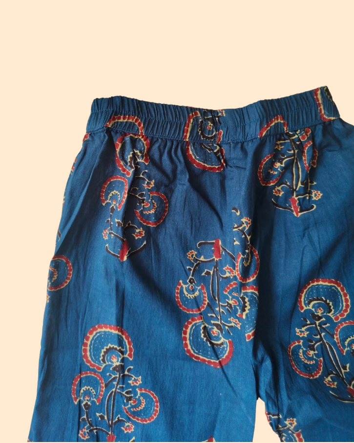 Blue cotton pajama pants with a red and gold paisley pattern, featuring an elastic waistband, shown against a solid beige background.