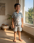 A toddler is wearing teal coloured camel printed shorts set standing near a window smiling