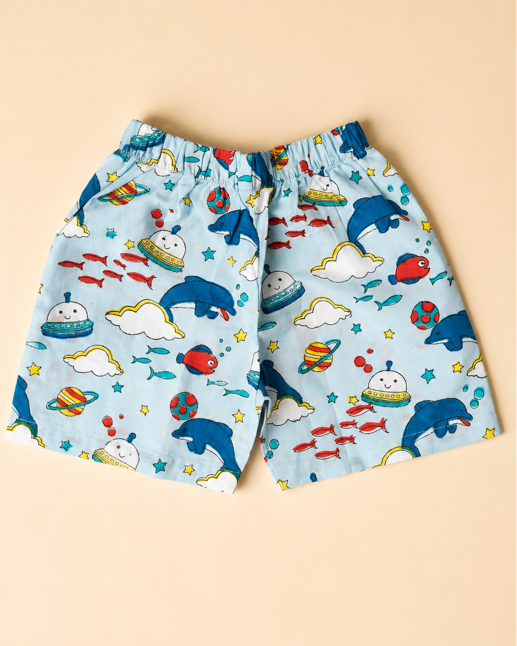 A cotton shorts with beautiful dolphin, rocket , clouds print on it from Aruvo is laid on beige background