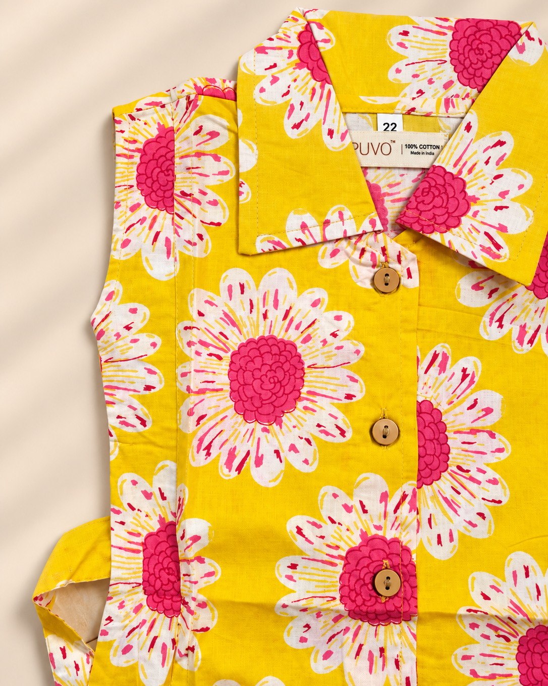 A folded yellow button-up shirt with a bold pink and white daisy floral print, featuring wooden buttons and a visible ARUVO brand label.