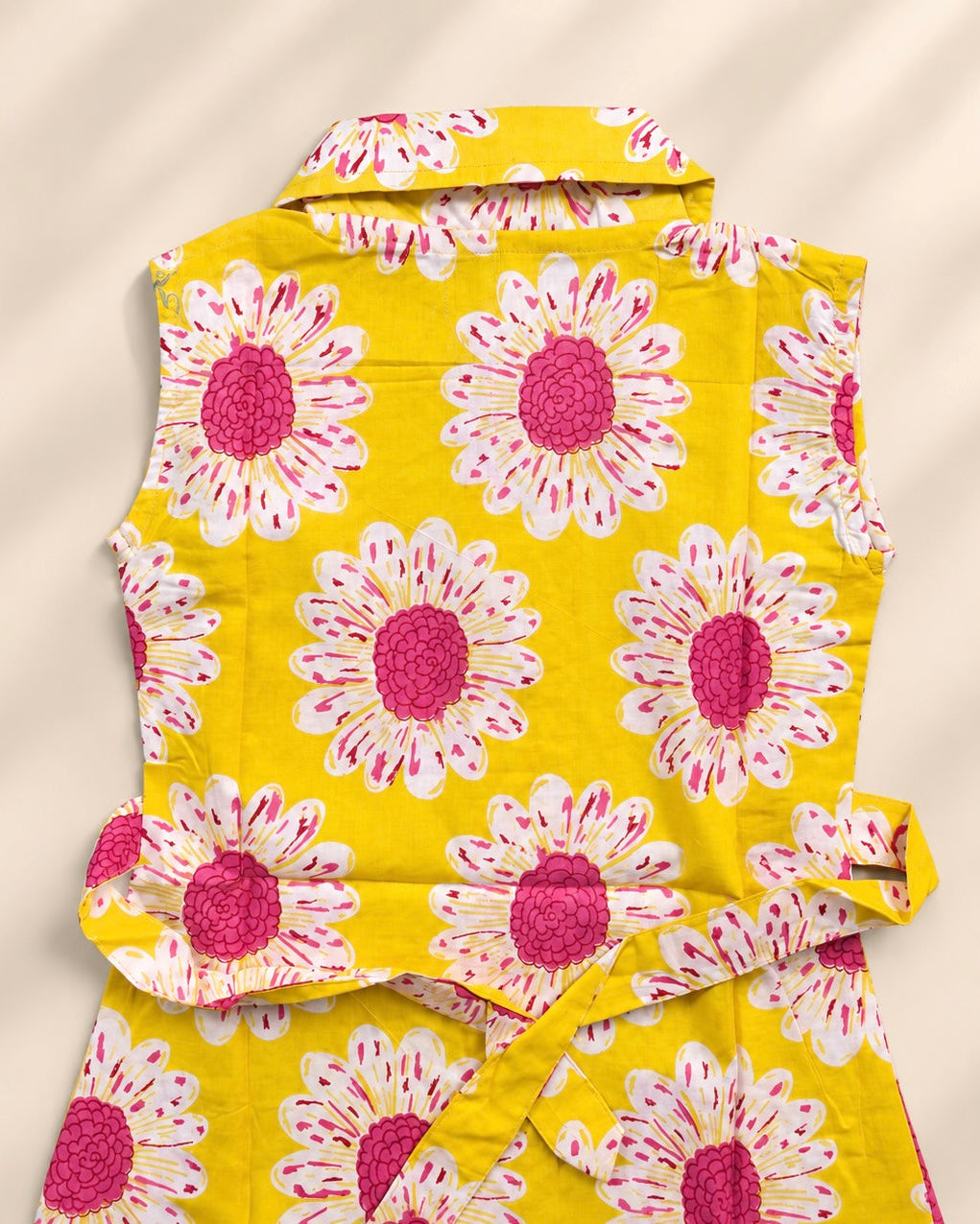 A sleeveless yellow top with a large pink and white daisy print, featuring a pointed collar shows back side of the dress 