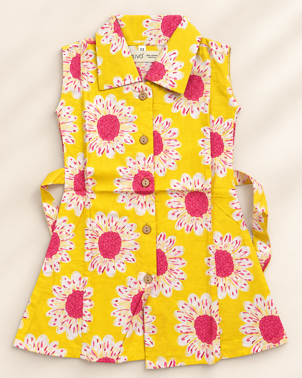 A sleeveless yellow button-front shirt dress with a large pink and white floral print, shown laid flat on a light beige background.