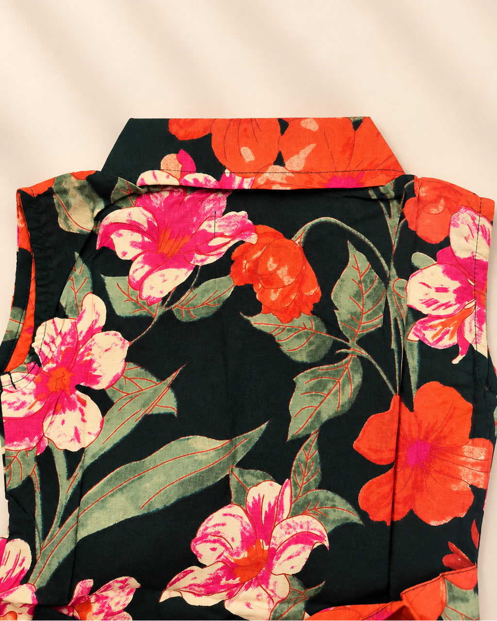 A close-up of a floral fabric garment laid flat on a light beige background. The fabric features a bold pattern of pink and orange flowers with green leaves on a black base.