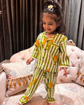 A young girl is wearing a striped green and beige color full sleeve nightsuit set from brand Aruvo, standing on a bed smiling 