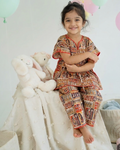 A young girl wearing a kaftan set crafted from 100% cotton from Aruvo, sitting on a table smiling 