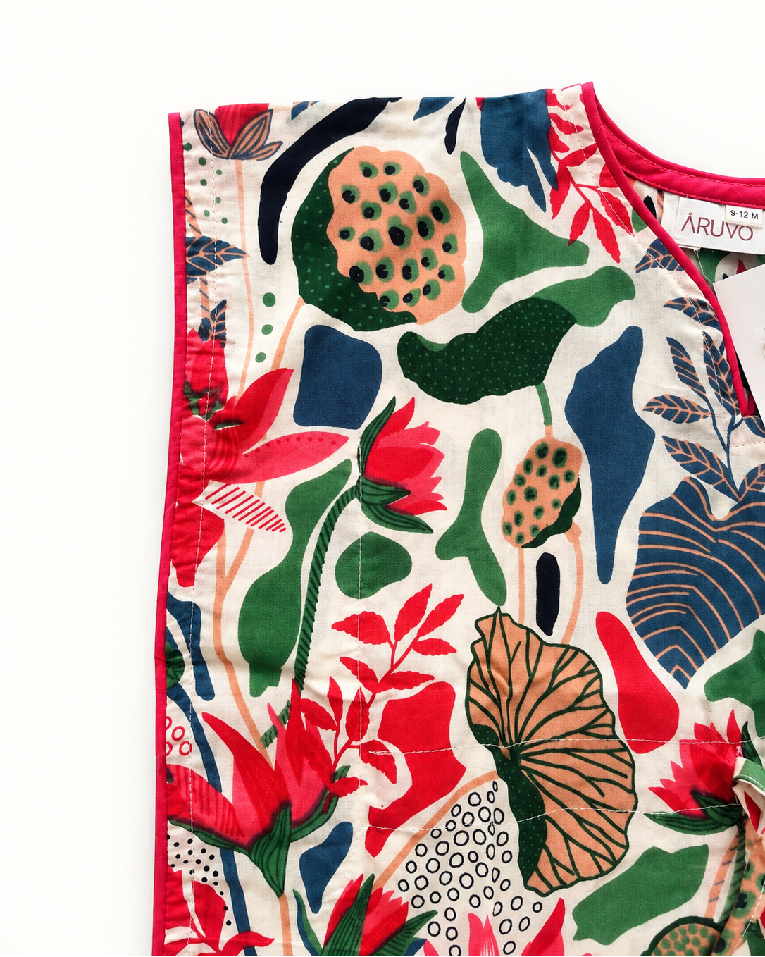 A close-up of a sleeveless top or dress by Aruvo, featuring a vibrant botanical print with red lotus flowers, green leaves, and blue abstract shapes on a cream background, with a red trim and a visible Aruvo brand label.