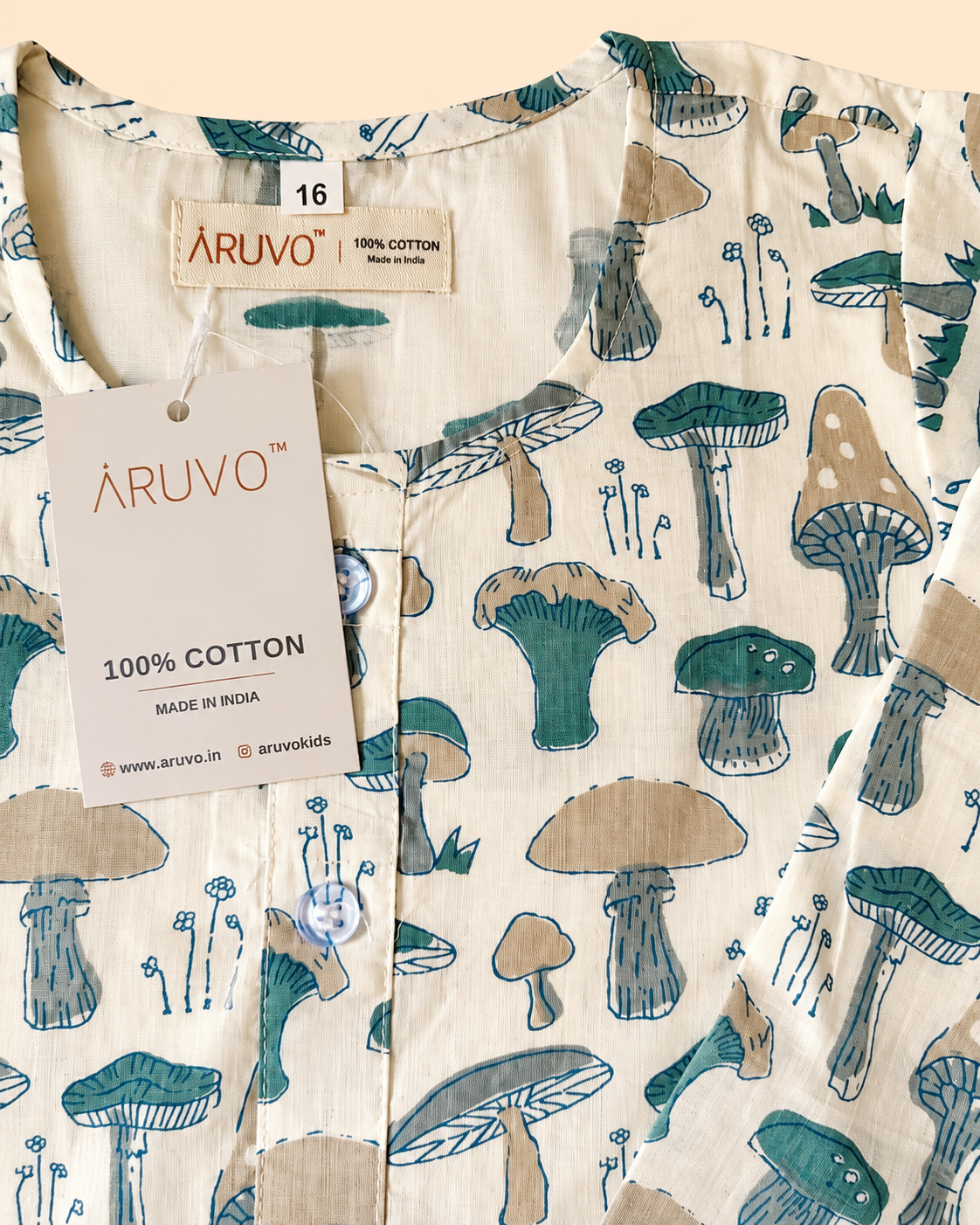 A close-up of a cotton garment with an all over mushroom print in teal, beige, and brown on a cream background. The brand label 'ARUVO' is visible inside the collar, and a hanging tag reads '100% COTTON MADE IN INDIA'.