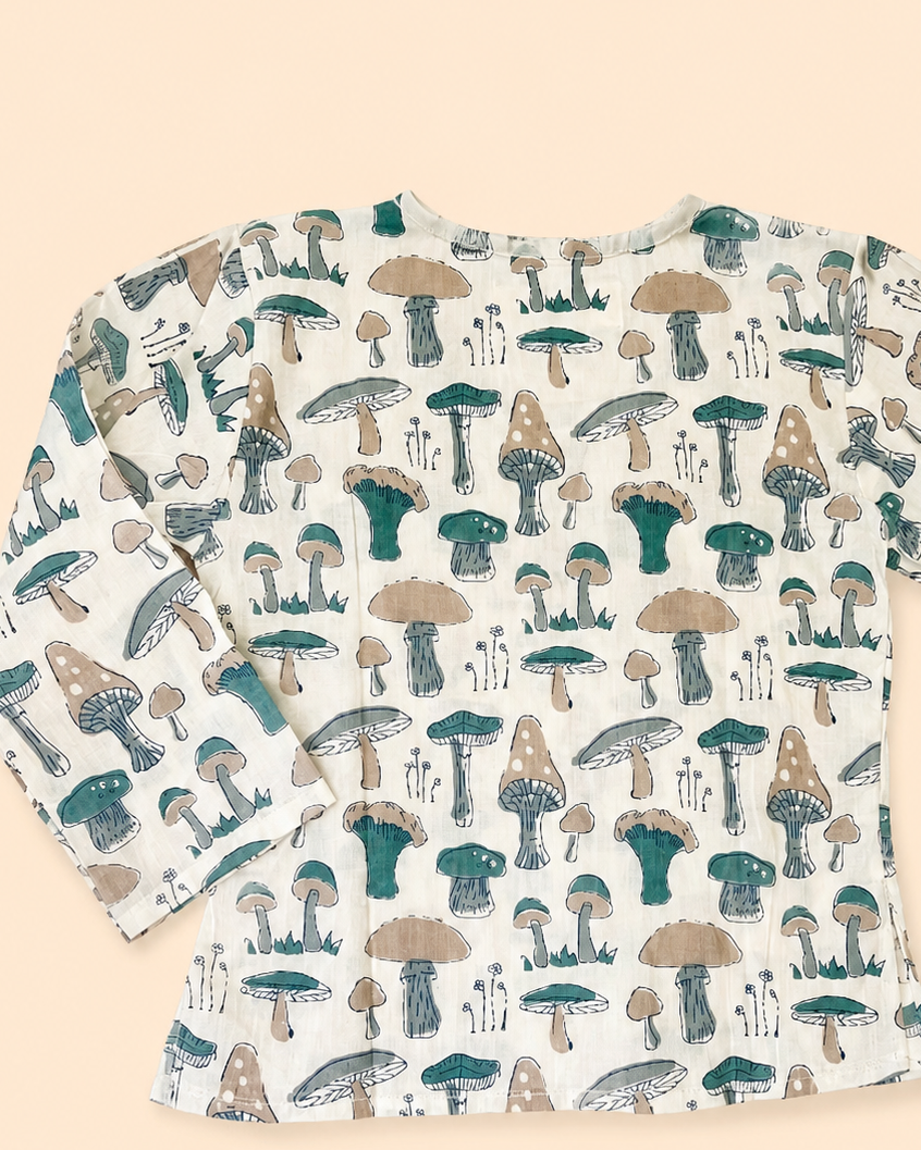 A long-sleeve white top show back side with an all-over mushroom print in teal and tan, laid flat on a solid pale peach background.