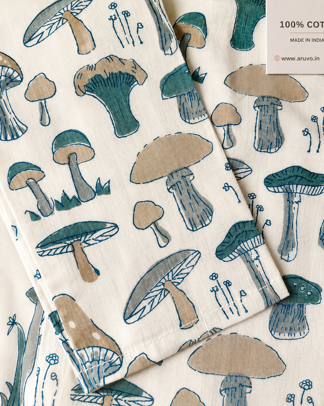 A close-up of a cotton fabric featuring a repeating mushroom print in teal, beige, and gray on an off-white background. 
