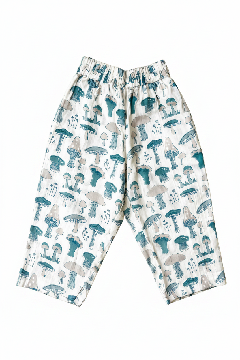 White wide-leg pants with an all-over mushroom print in teal and gray, featuring an elastic waistband, laid flat on a solid pale yellow background.