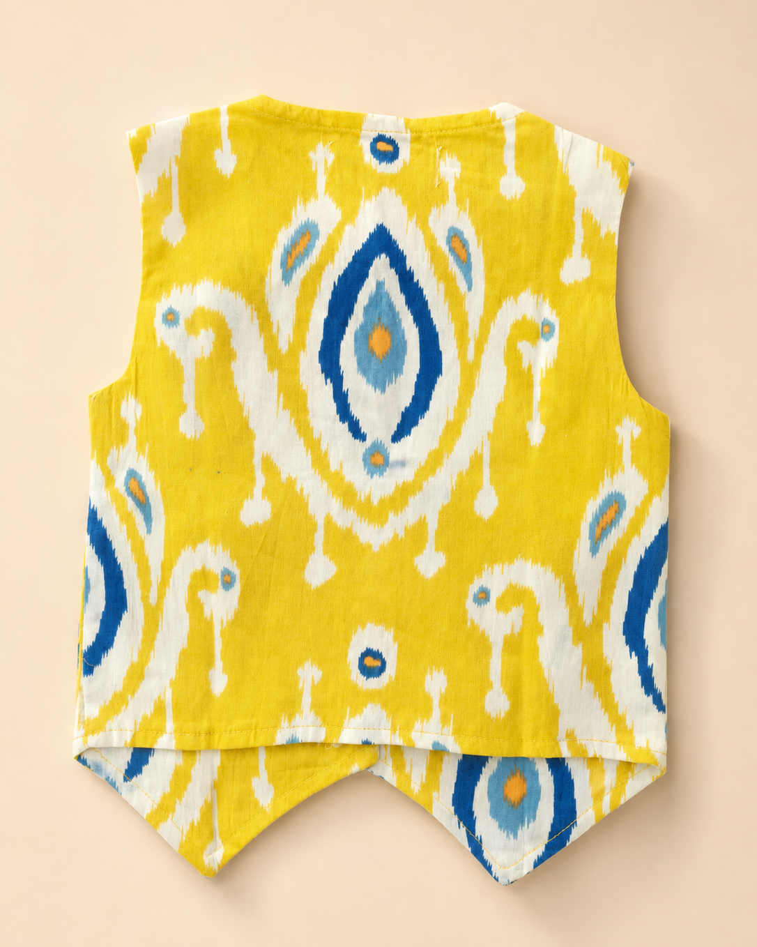 A sleeveless yellow vest with a blue and white ikat pattern show back side, laid flat on a light beige background.