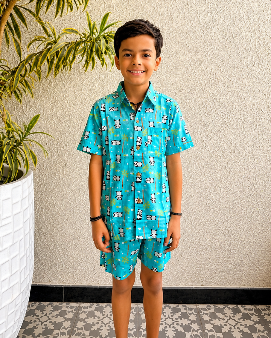 Child wearing Aruvo's blue patterned outfit, Panda prints on it standing in front of a textured wall with a plant.