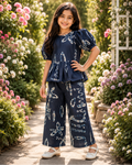 Young girl in a navy blue outfit with white patterns, from Aruvo standing in a garden with flowers.