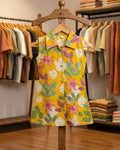 Yellow floral sleeveless shirt dress on a wooden hanger with a clothing store background.